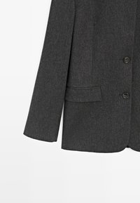 Szary wełniany żakiet z guzikami, pojedyncza kieszeń. Dopasowany fason, wyraźnie zarysowane ramiona i gładka tekstura. Widoczne detale przeszycia.
