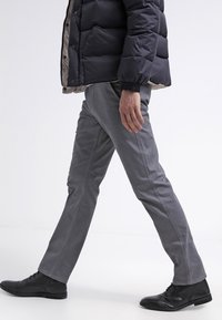 Graue, eng anliegende Hosen mit glatter Textur, schmal zulaufendem Bein und gesteppten Details, kombiniert mit schwarzen Schuhen und einer dunklen Steppjacke.