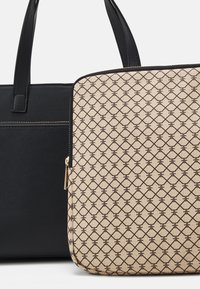 Czarna syntetyczna torba tote obok beżowego etui na laptopa z geometrycznym wzorem i złotym suwakiem. Gładka tekstura i wyraźnie zarysowany kształt.