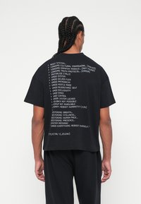 Μαύρο oversized t-shirt με λευκό κείμενο σε μορφή κώδικα στην πλάτη. Το ύφασμα φαίνεται μαλακό, με χαλαρή εφαρμογή και κοντά μανίκια.