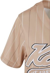 Tan Baseball-Trikot mit weißen Streifen, kurzen Ärmeln und einem großen gestickten Logo in kontrastierenden Farben auf der Vorderseite.