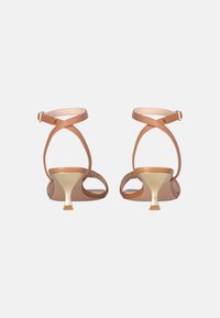 Sandali in pelle marrone con sottili cinturini alla caviglia, punta aperta e tacco metallico dorato a punta. Design minimalista con una texture liscia.