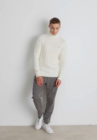 Witte kabelbrei turtleneck trui gecombineerd met grijze broek en witte sneakers, met een aansluitend ontwerp en geribde mouwen.