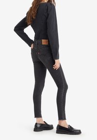 Jeans negros de tiro alto y corte ajustado con dobladillo sin acabar, que presentan un parche de cuero en la parte trasera, combinados con mocasines negros.