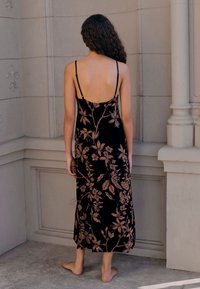 Vestito nero a fiori con spalline sottili, caratterizzato da un delicato motivo botanico color oro rosa e una lunghezza fino a metà polpaccio, mostrato di schiena.