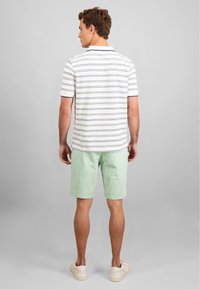 Hvite og marineblå stripete polo-skjorte med korte ermer, parret med lyse grønne shorts, brukt med beige sneakers. Enkelt design, uformell passform.