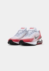 Scarpe sportive con tomaia in rete bianca traspirante, con dettagli in gradiente rosso e suola nera. Notevole il logo Nike e il design della linguetta imbottita.