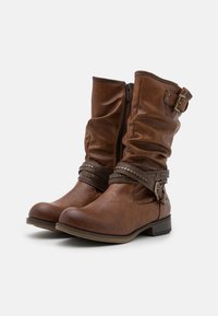Bottes en cuir marron à la cheville avec un design drapé, des accents à boucle, des clous en métal sur une sangle et une fermeture éclair sur le côté. Talon plat et bout rond.