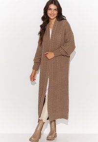 Długi kardigan z otwartym przodem w jasnobrązowym dzianinowym materiale o fakturowanym wzorze, z opadającymi ramionami i ściągaczami przy mankietach.