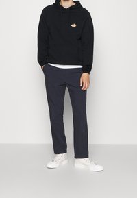 Felpa nera con cappuccio, tasca frontale e dettagli del logo, abbinata a pantaloni blu navy e sneakers bianche. Design leggero e informale.