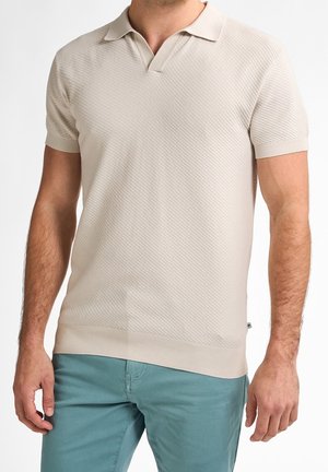 Beige kortærmet polo skjorte med et struktureret skrå mønster, der har en V-hals og ribbet kant, parret med teal bukser.