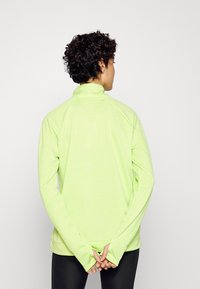 Langärmliger Pullover mit hohem Kragen in leuchtendem Neon-Grün, der eine glatte Textur und subtile reflektierende Details auf der Rückseite aufweist.