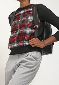 Czarny sweter z długim rękawem w czerwono-czarną kraciastą wzór z logo "GAP". Połączony z jasnoszarymi spodniami plisowanymi i czarnym plecakiem.