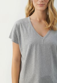 Grå V-ringad t-shirt med korta ärmar, mjukt bomullstyg, avslappnad passform, subtil struktur och sömdetaljer vid halsringningen.