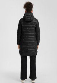 Must mustavillane parka, millel on kapuuts, stepitud disain, põlvepikkune, horisontaalse õmblusega ja avara lõikega, koos tumedate laienevate pükstega.