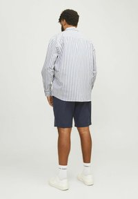 Striped long-sleeve shirt in white and navy, paired with navy shorts. Model is wearing white sneakers and ankle socks.