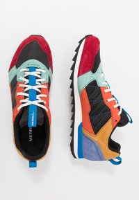 Färgglada sneakers med svarta, röda, orange, mintgröna och blå mockadetaljer, vita snören och en robust svart sula med en blå accent.