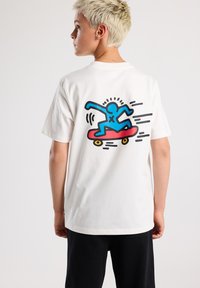 White cotton t-shirt featuring a colorful graphic of a blue figure skateboarding in red on the back, with motion lines in black.