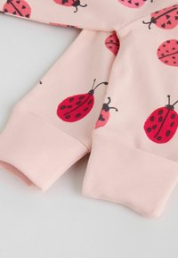 Primer plano de mangas de tela rosa con estampados de mariquitas rojas y negras y puños acanalados sobre un fondo claro.
