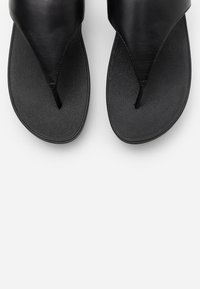 Černé žabky s hladkým koženým svrškem, texturovanou podrážkou a minimalistickým designem, zdůrazňující thong styl a štíhlý tvar.