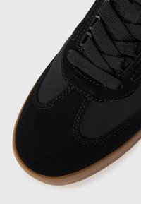 Black athletic shoe with a suede upper and nylon accents. Features a rubber sole, flat laces, and stitched detailing. Minimalist design.
