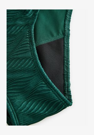 Tessuto di un verde scuro con texture e motivi a onda, combinato con un materiale nero liscio di lato, presenta bordi cuciti per una maggiore durata.