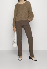 Bruine gebreide trui, beige coltrui, bruine op maat gemaakte broek, witte ronde handtas en tweekleurige schoenen met blokhak.