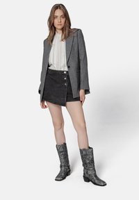 Gray wool blazer over a white blouse with lace detailing, paired with a black denim skirt and knee-high gray boots with metallic accents.