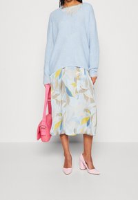 Jasnoniebieski sweter dzianinowy, spódnica midi w kwiatowy wzór w niebiesko-żółtych odcieniach, różowa torba oraz jasnoróżowe szpilki. Przytulny, warstwowy look.