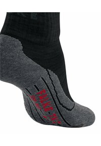 Calcetín negro con suela texturizada gris que presenta patrones antideslizantes y la marca "Falke" en rojo. Diseño de altura hasta el tobillo con parte superior acanalada.