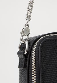 Black textured bag with a silver chain strap, featuring a zip closure and metal hardware. The material has a patterned surface.