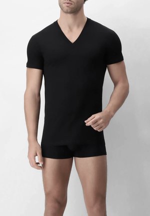Uomo che indossa una maglietta nera aderente a maniche corte con scollo a V e boxer neri abbinati, su uno sfondo semplice.