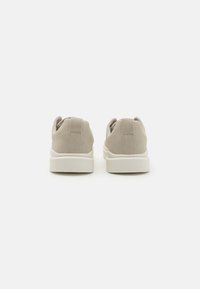 Beige Wildledersneaker im Low-Top-Design mit einer weißen Gummisohle und Rückziehlaschen für einfaches An- und Ausziehen. Glatte Oberfläche und minimales Design.