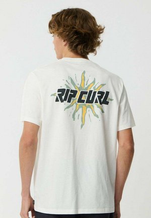 Jong persoon met lichtbruin golvend haar draagt een wit T-shirt met de tekst "RIP CURL" en een kleurrijk zonnestraalontwerp op de rug.