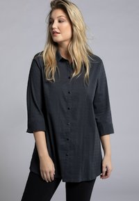 Camicia nera con bottoni, realizzata in un tessuto testurizzato, dalla vestibilità comoda e con maniche a tre quarti. Caratterizzata da un colletto a punta e chiusura frontale con bottoni.
