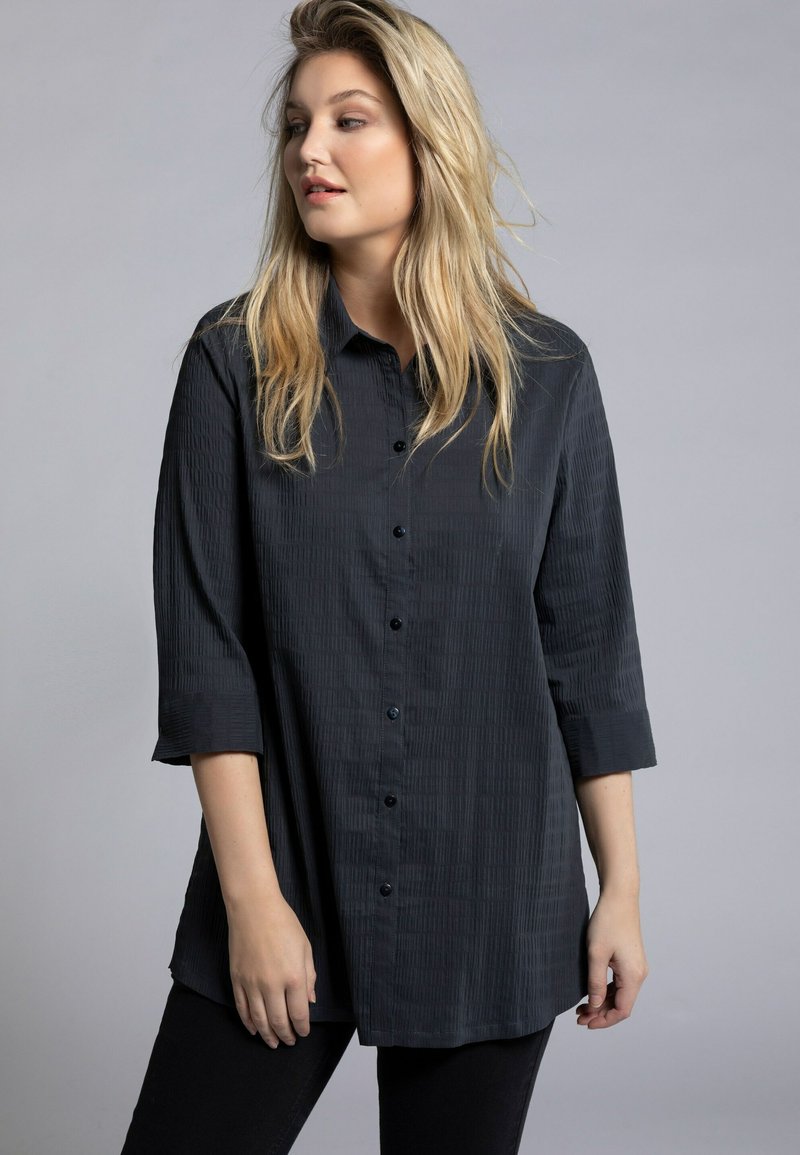 Camicia nera con bottoni, realizzata in un tessuto testurizzato, dalla vestibilità comoda e con maniche a tre quarti. Caratterizzata da un colletto a punta e chiusura frontale con bottoni.