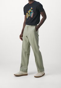 Czarny t-shirt z kolorową grafiką roweru, w połączeniu z jasnoszarymi spodniami z plisami i białymi trampkami o teksturowanej podeszwie.