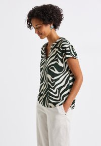 Green and white short-sleeve blouse with a zebra pattern, featuring a V-neck and relaxed fit, paired with cream wide-leg trousers.