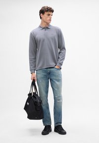 Szara, długorękawowa koszulka polo z kołnierzykiem, zestawiona z jasnobłękitnymi dżinsami w stylu vintage. Czarna torba z logo i czarne sneakersy.
