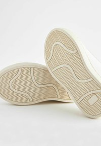 Krémové podrážky bot s vlnkovou texturou a podrobnými vzory pro lepší uchopení. Zaoblené okraje a jemné křivky zlepšují design.