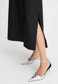 Robe midi noire avec fente latérale associée à des talons aiguilles argentés métalliques munis de brides à la cheville et d'un design épuré.