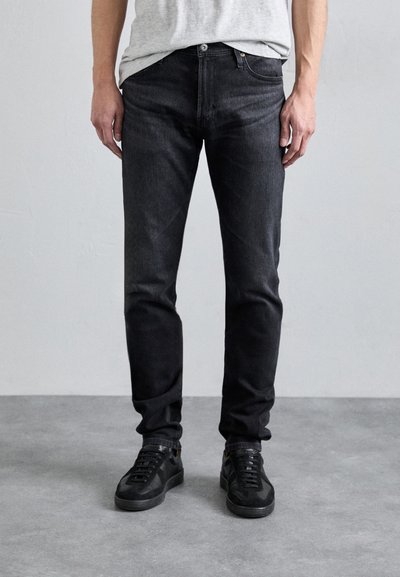 Černé džíny z denimu s úzkým střihem, které mají klasický design s pěti kapsami a jemnou texturou. V kombinaci s černými teniskami.