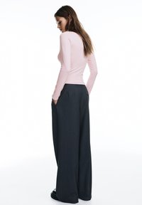 Top roz pal cu mâneci lungi, combinat cu pantaloni largi de culoare gri închis, cu talie înaltă. Pantalonii au buzunare laterale și un aspect croitorit.