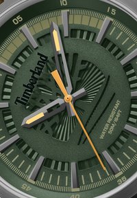 Reloj analógico verde con un dial texturizado, acentos en plata y oro, que presenta marcadores de hora en negrita y un distintivo logo de Timberland. Resistente al agua hasta 50 metros.