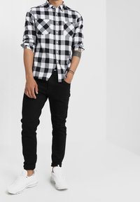 Zwart-wit geruit flanellen overhemd met twee borstzakken, gecombineerd met een zwarte broek en witte sneakers, wat een casual uitstraling geeft.