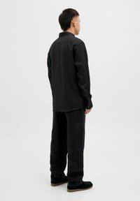 Camisa de lino negra con cuello y mangas largas, combinada con pantalones holgados a juego y zapatos negros, vista desde la parte posterior.