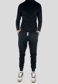 Černé tričko s dlouhým rukávem, slim fit, v kombinaci s černými tepláky s šedým tkaničkovým páskem. Obuv je černobílá s barevnými akcenty.