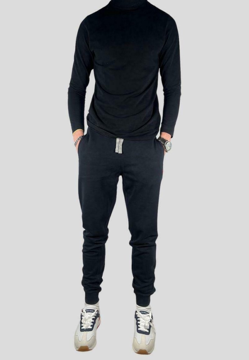 Černé tričko s dlouhým rukávem, slim fit, v kombinaci s černými tepláky s šedým tkaničkovým páskem. Obuv je černobílá s barevnými akcenty.