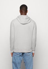 Sudadera gris con capucha hecha de tela suave, con bolsillo tipo canguro, puños acanalados y dobladillo recto. Se lleva con jeans de mezclilla azul.