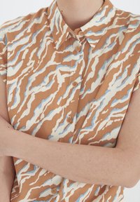 Braun- und cremefarbener Kurzarmhemd mit einem wellenförmigen blauen und weißen Muster, ausgestattet mit einer Knopfleiste und einem klassischen Kragen.